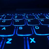 An illuminated computer keyboard. Glowing blue in the dark.